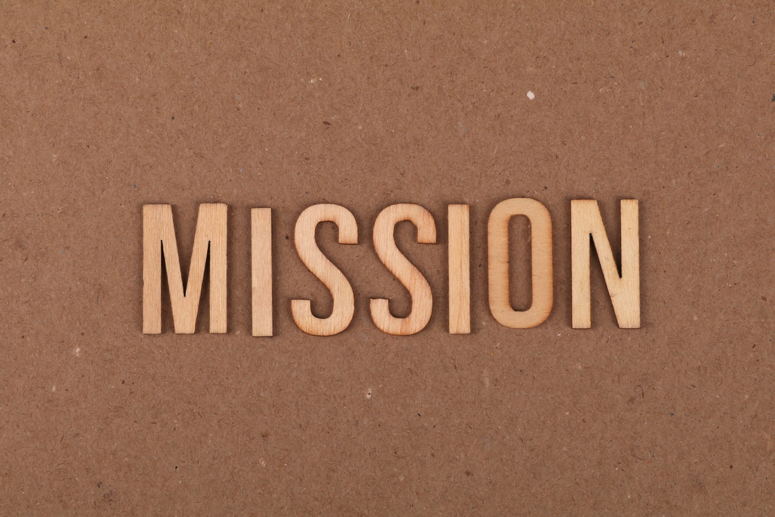 Wooden letters spelling 'MISSION' on textured cardboard background, emphasizing goals and purpose.