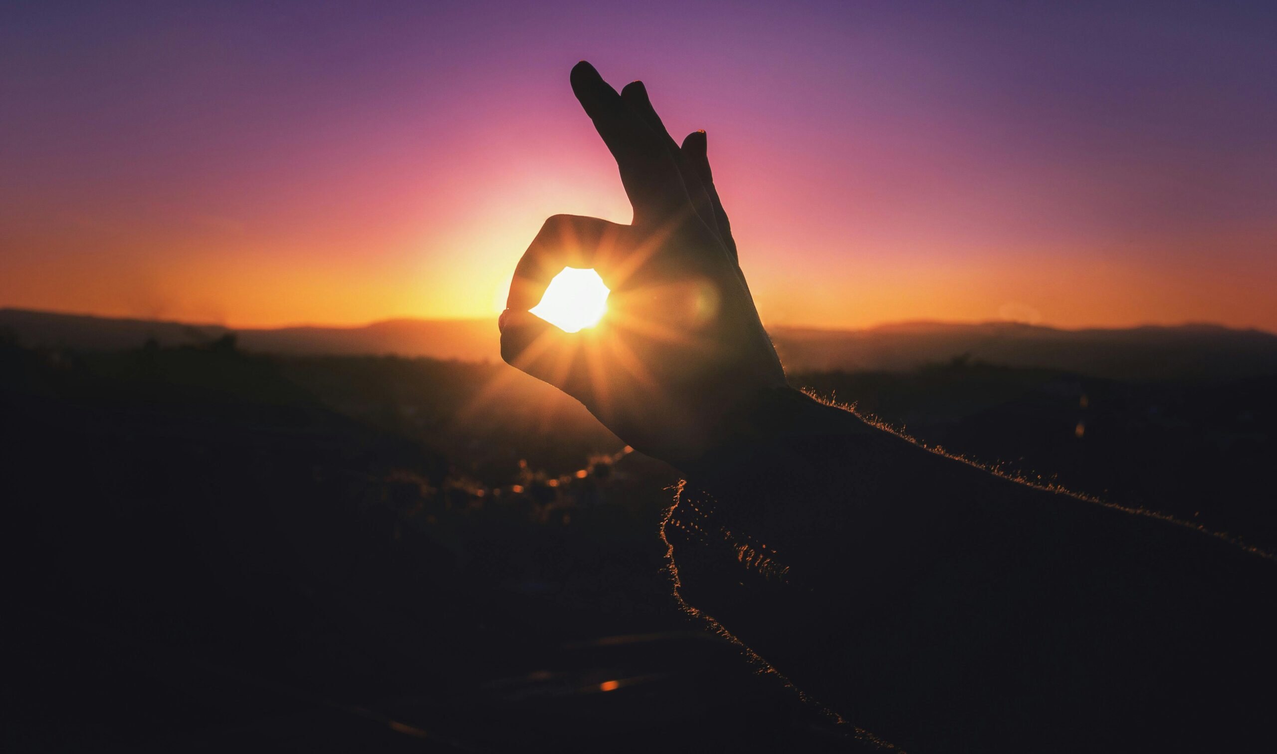 Silhouette of a hand framing the setting sun during a vibrant sunset, capturing a creative moment.